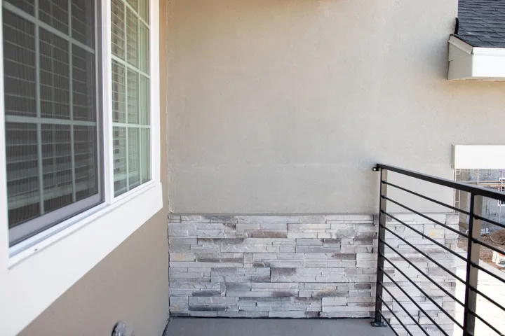 Exterior balcony featuring a modern horizontal bar railing, stucco walls, and a stacked stone accent wall