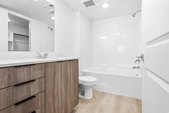 Bathroom featuring a wood-finish vanity with a light-toned countertop, a full-width mirror, and a white tub/shower combination
