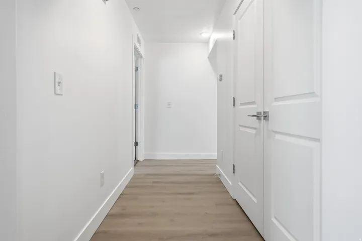 Hallway featuring wood-finish flooring, white walls, white baseboards, and white paneled doors with brushed nickel hardware