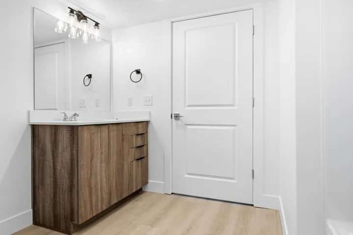 Bathroom featuring a wood-finish vanity with an integrated sink and light countertop, chrome faucet, and rectangular wall mirror