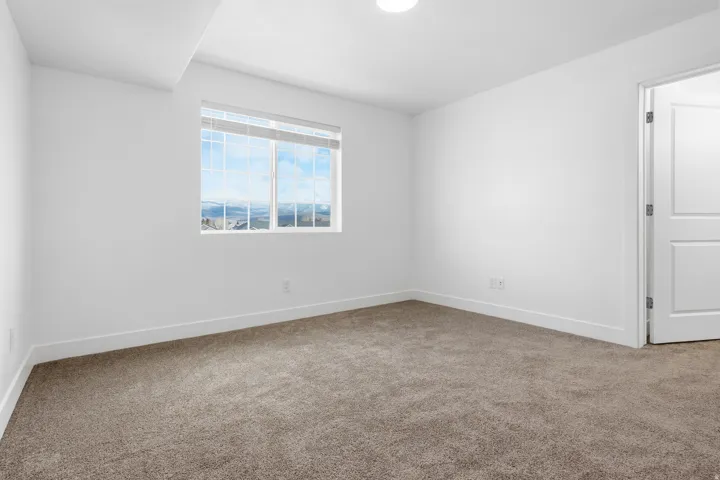 Bright room featuring a large window with white blinds, neutral carpet, and white walls