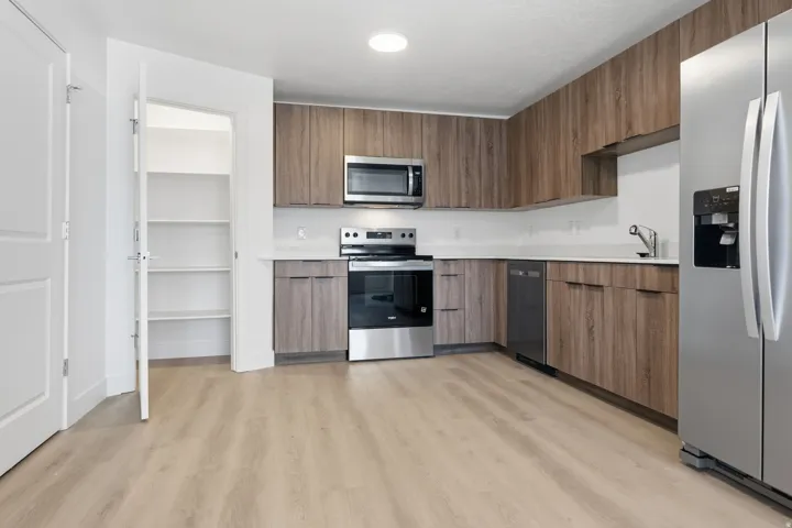 Modern kitchen featuring wood-finish cabinetry, stainless steel appliances, white countertops, and light wood-finish flooring