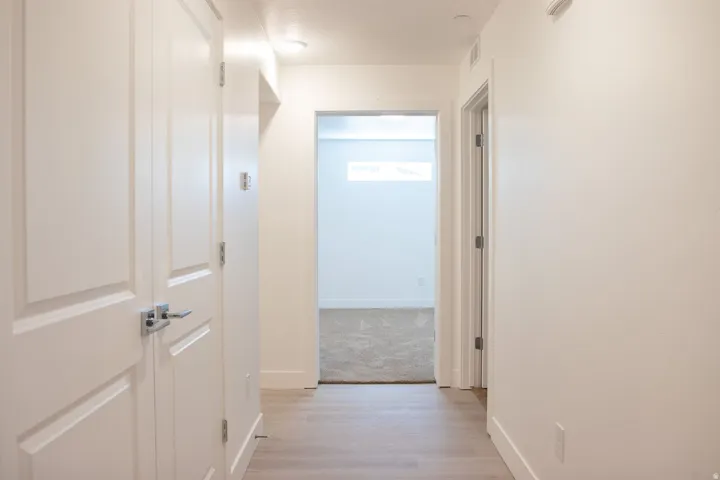 Hallway featuring light wood-finish flooring, white walls, recessed lighting, and white paneled doors with chrome hardware