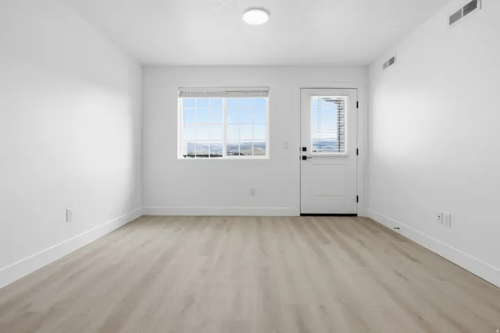Spacious room featuring light wood-finish flooring, white baseboards, and bright white walls