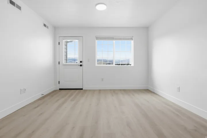 Spacious room with light wood-finish flooring, white walls, and a white egress door with an integrated window blind