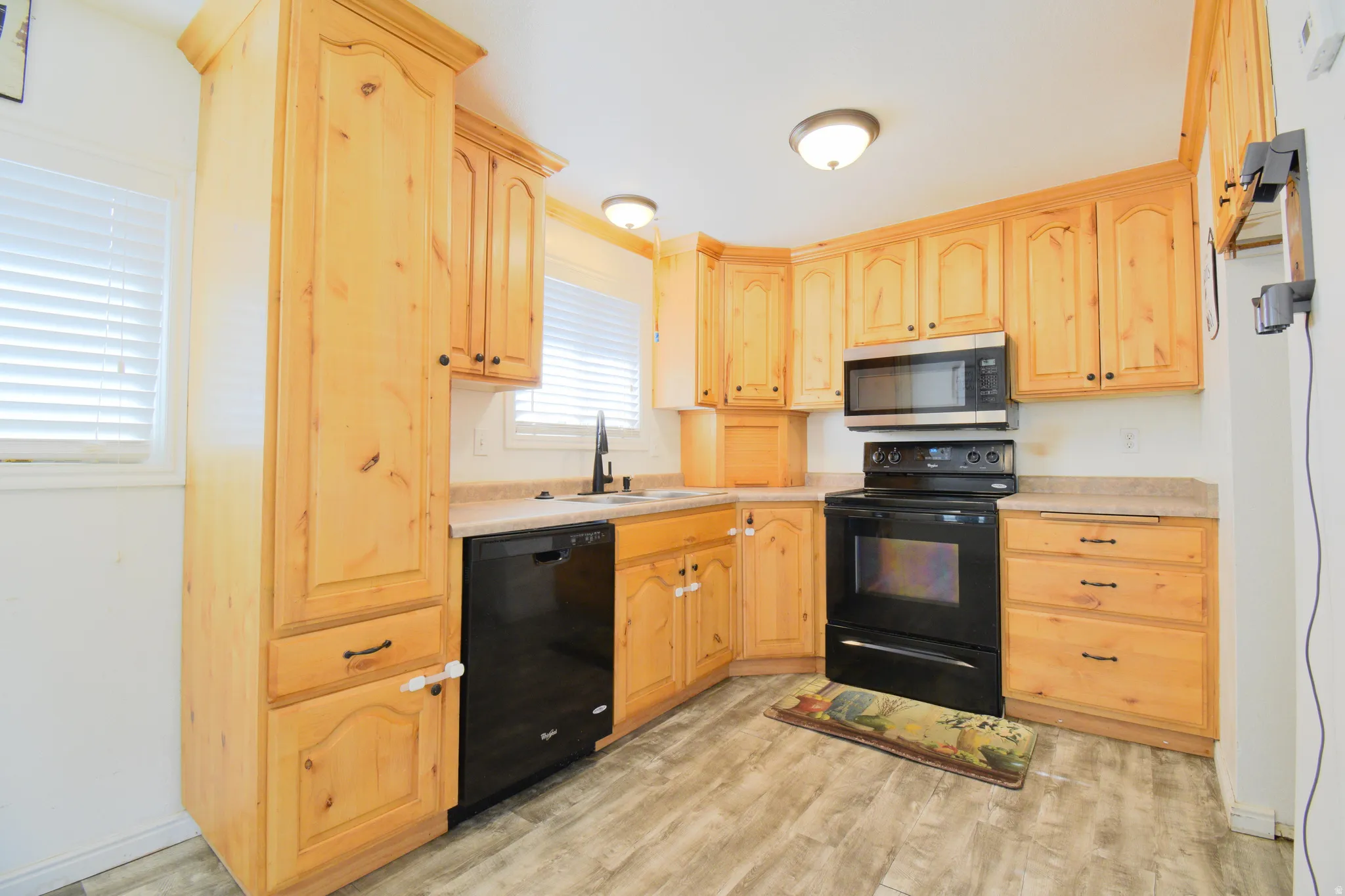 Kitchen featuring light wood cabinetry, black appliances, light-toned countertops, and wood-finish flooring