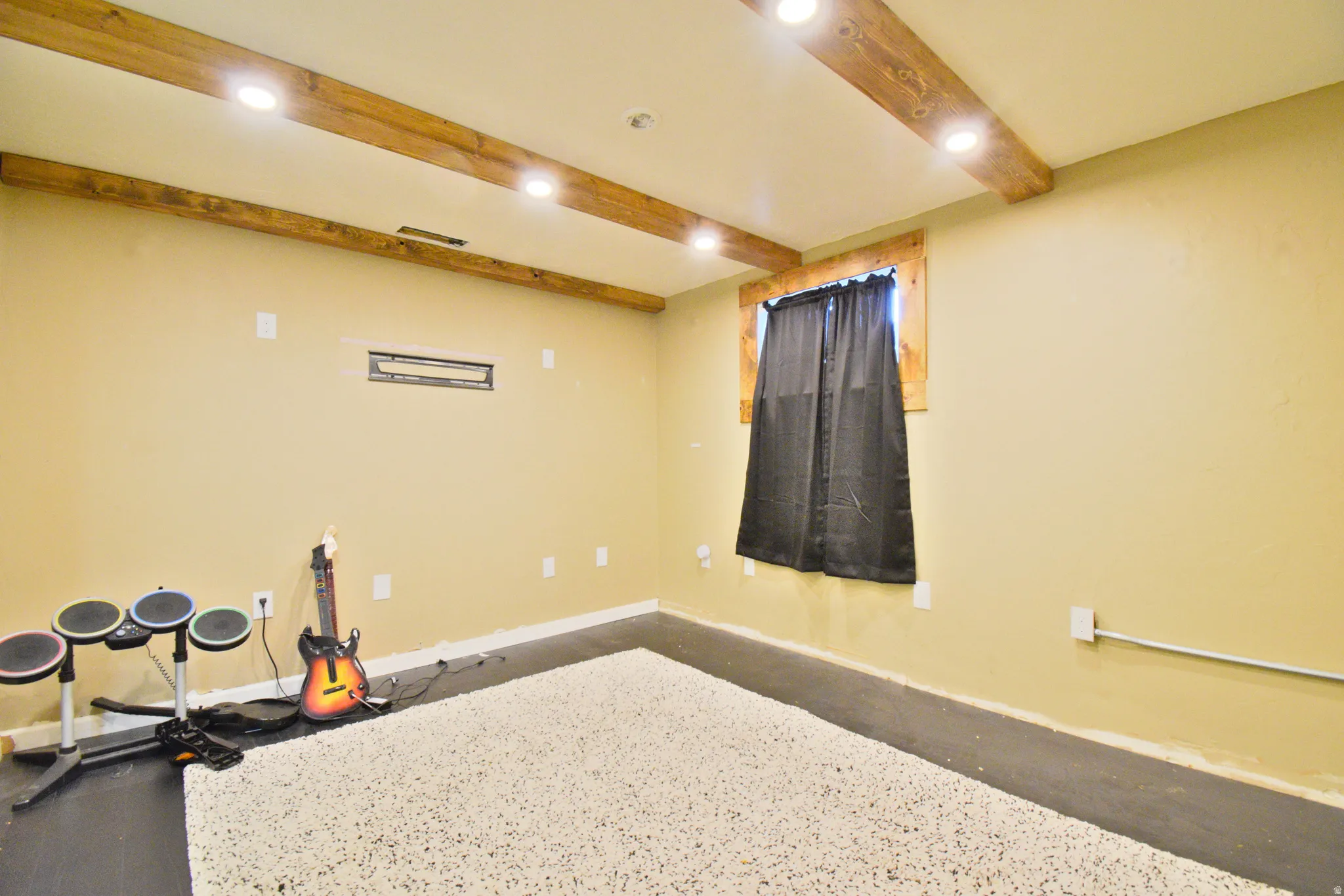 Finished room featuring exposed wood ceiling beams with recessed lighting, a wood-framed window, and a built-in wall niche