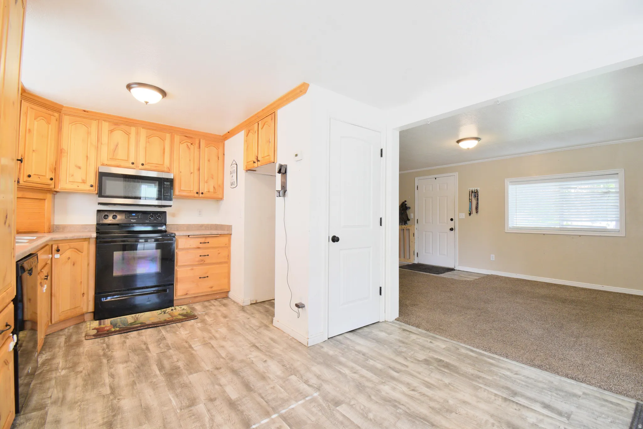 Kitchen featuring wood cabinetry, stone-look countertops, black appliances, and wood-finish flooring