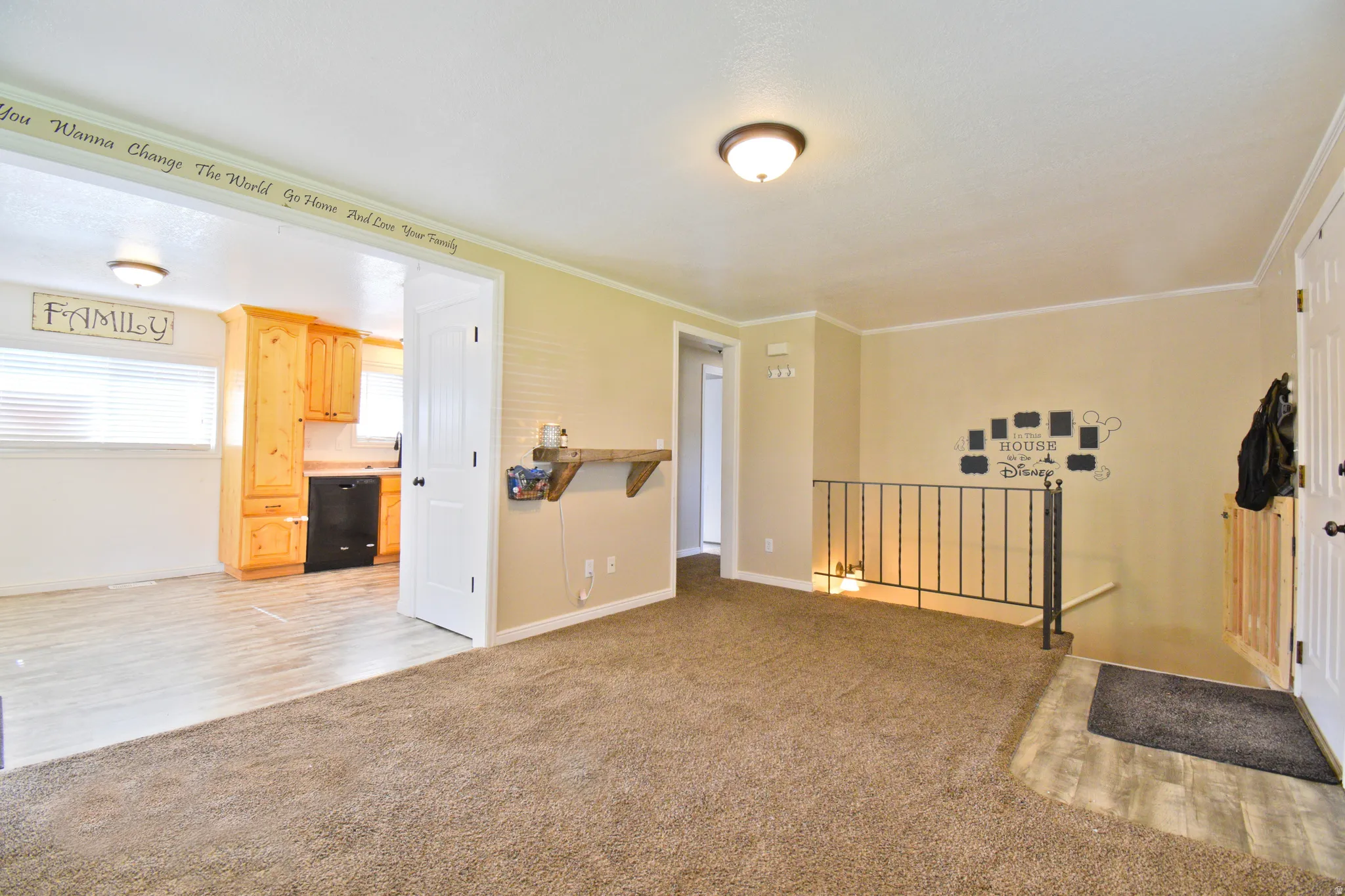 Open-concept interior featuring carpet and wood-finish flooring, a wrought iron railing, and a doorway leading to a kitchen with wood cabinetry and black appliances