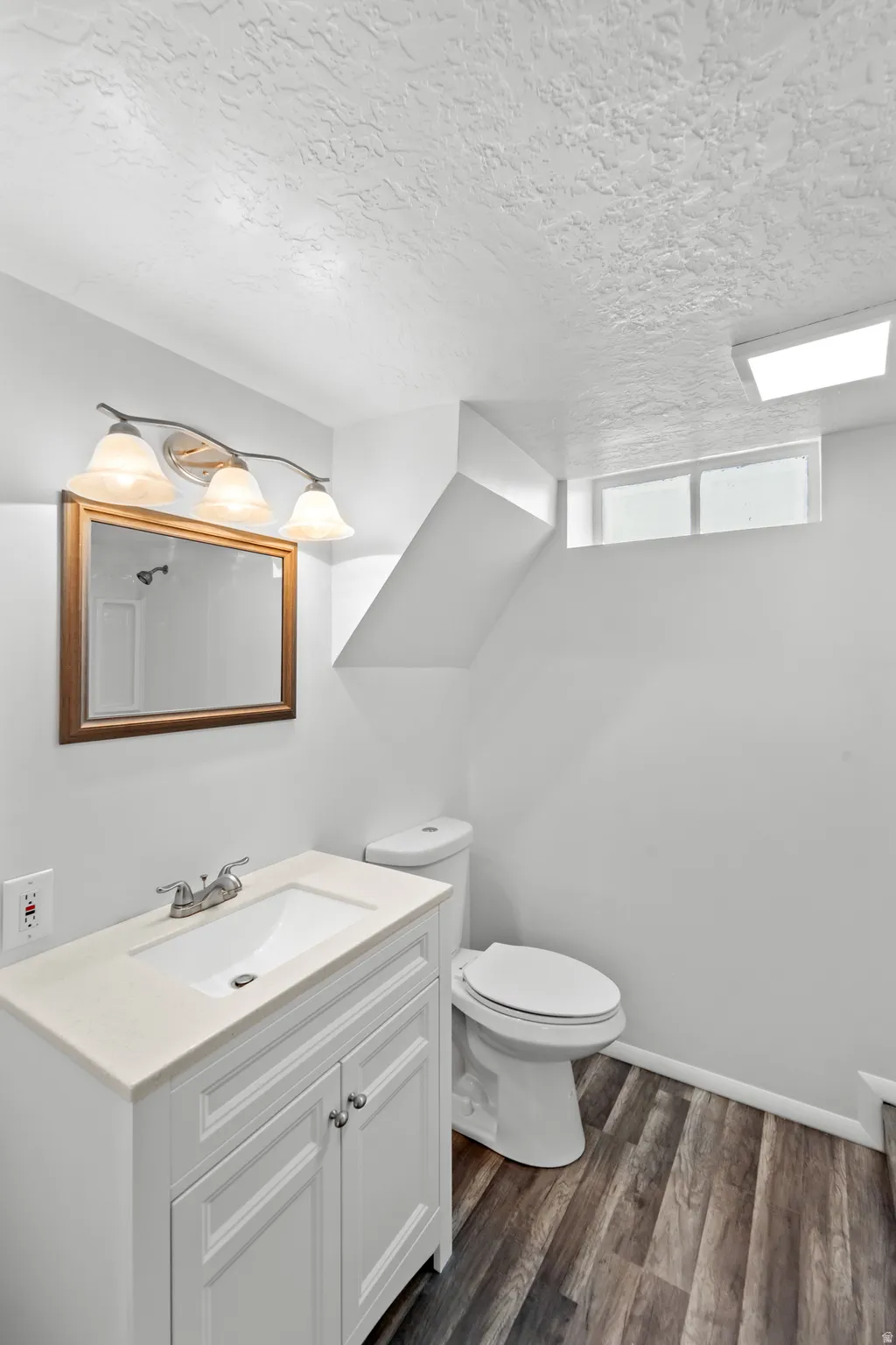 Bathroom featuring a white vanity with an integrated sink, polished chrome faucet, wood-finish flooring, and a window for natural light
