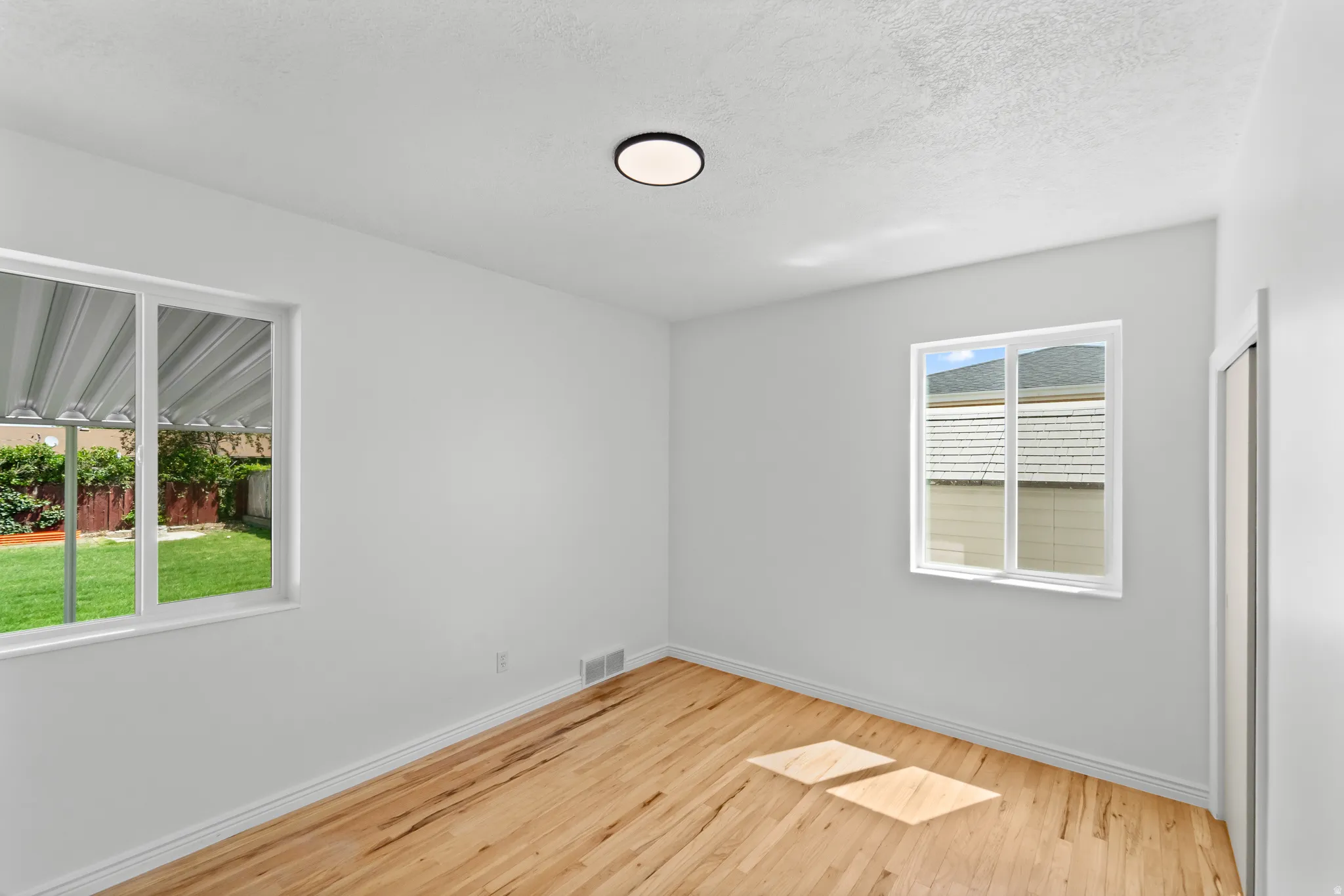 Bright room with natural wood-finish flooring, two windows, a ceiling-mounted light fixture, and white baseboards