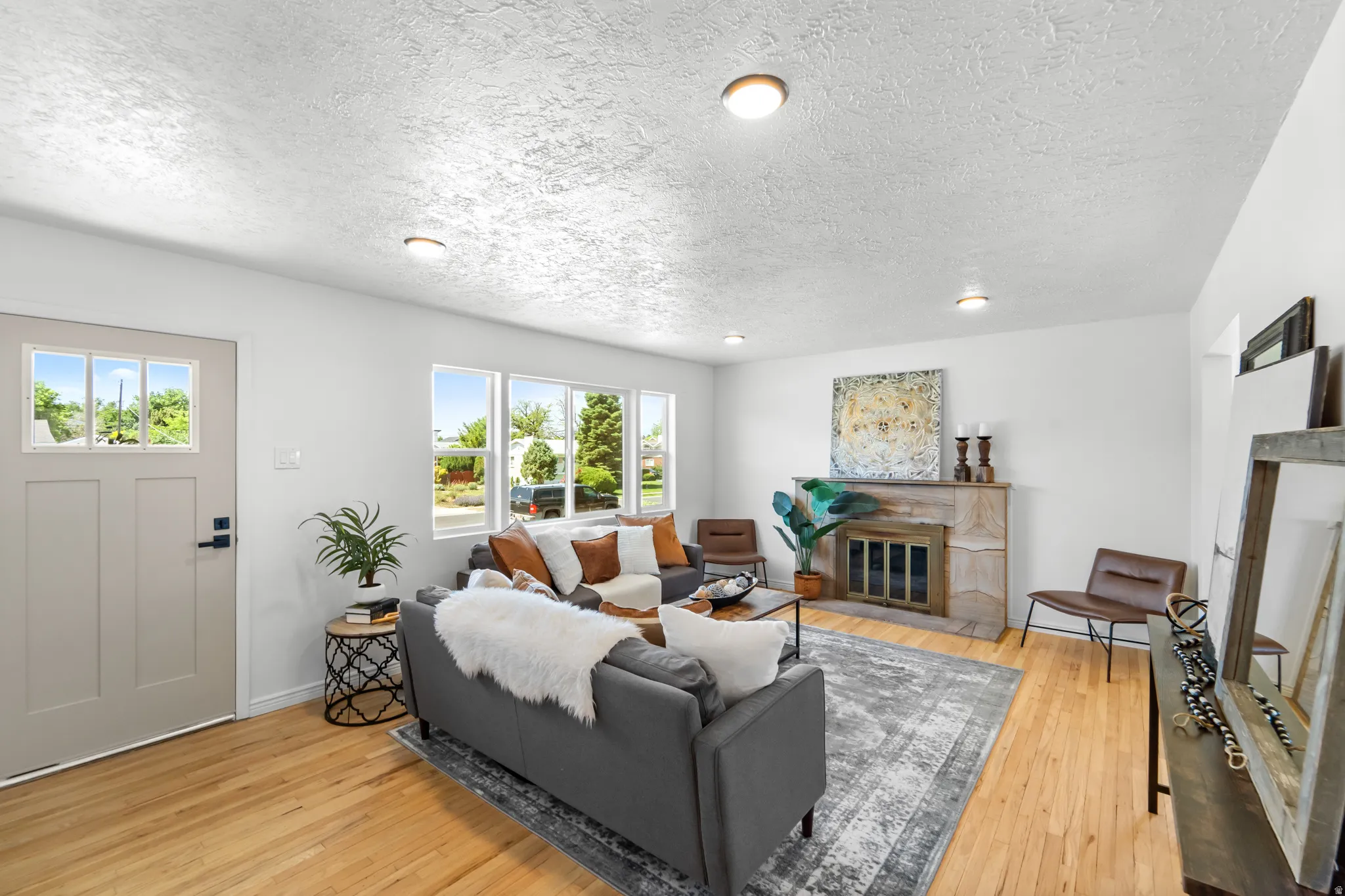 Living area featuring wood-finish flooring, a stone fireplace, recessed lighting, and multiple windows