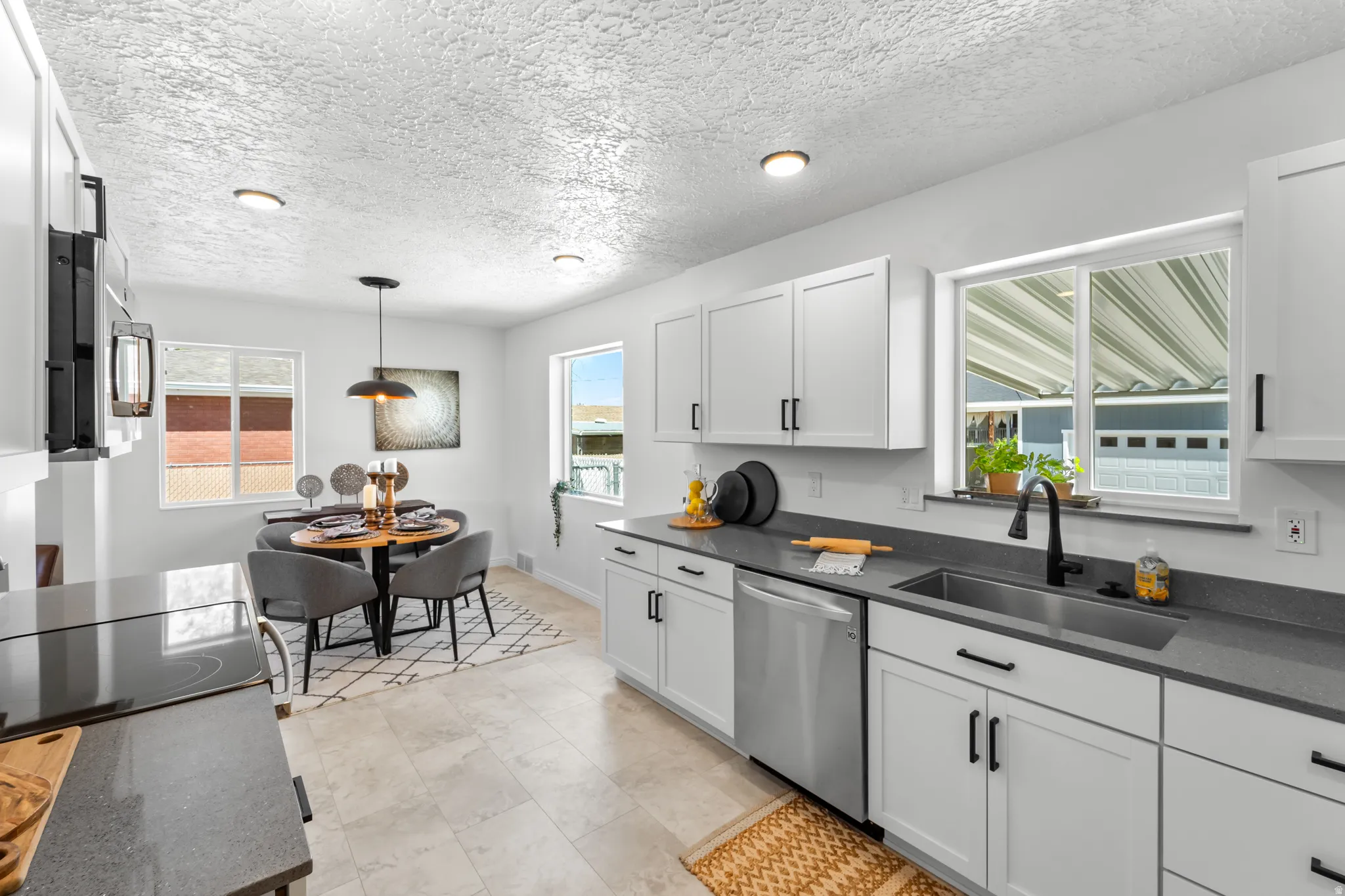 Open-concept kitchen featuring white cabinetry, dark countertops, a stainless steel dishwasher, and a stainless steel sink with a matte black faucet