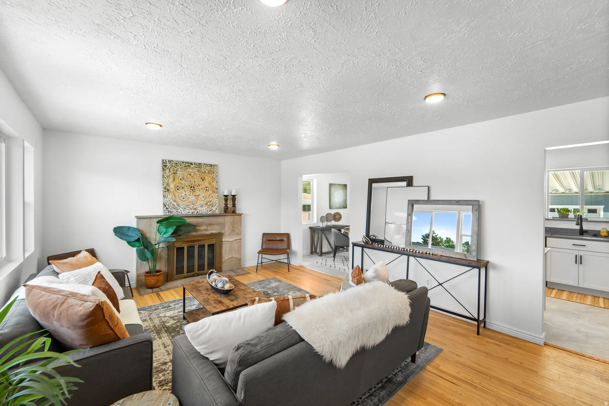 Bright living area featuring wood-finish flooring, a stone-clad fireplace, and white walls