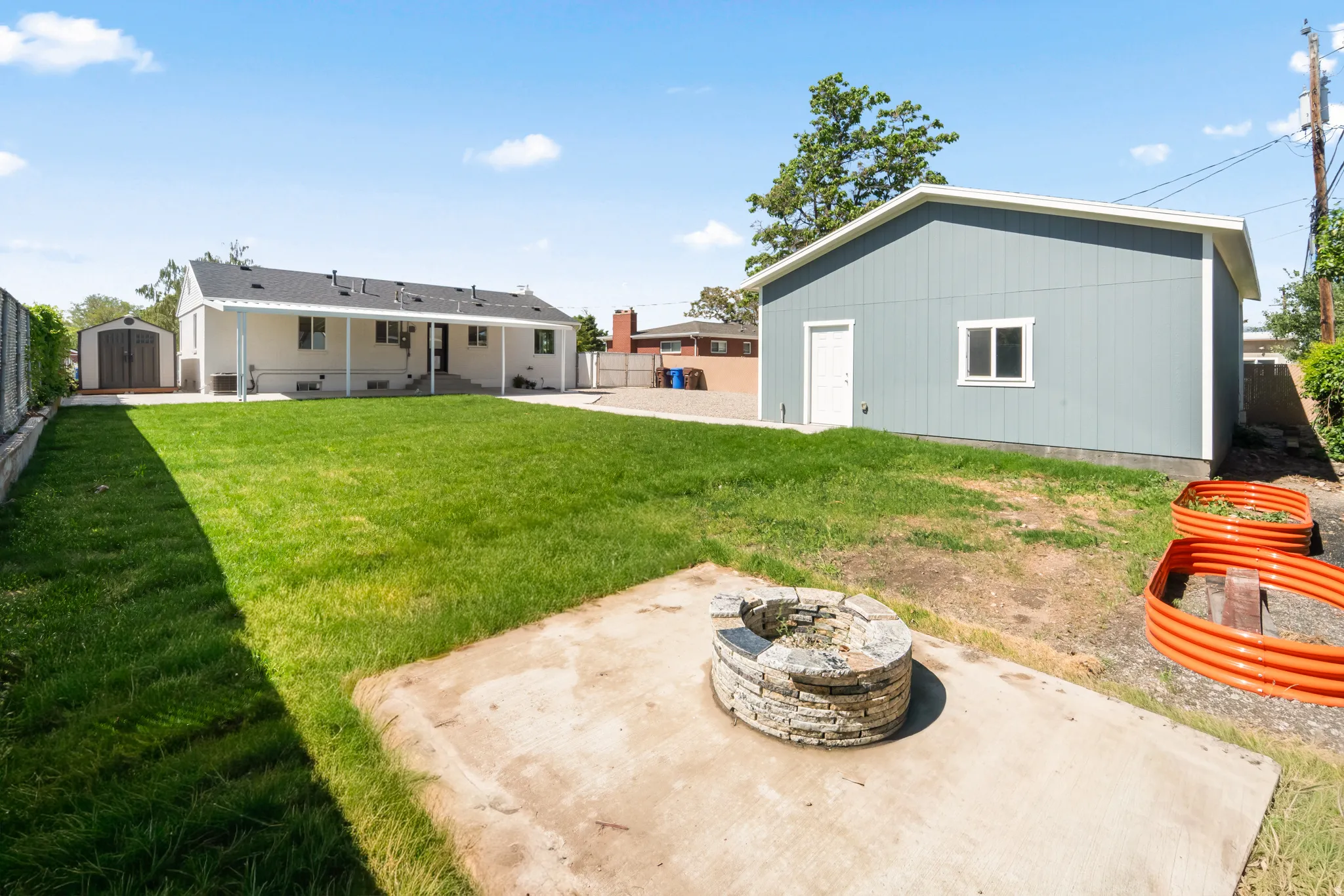 Expansive backyard featuring a stone fire pit, a large detached structure with siding, and a covered back patio on the main residence