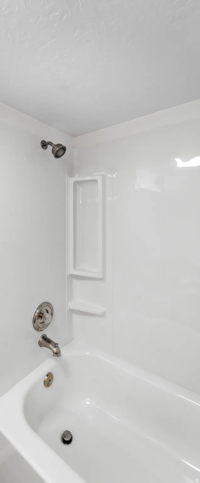 White bathtub and shower combination featuring a built-in shelving niche and brushed nickel shower fixtures