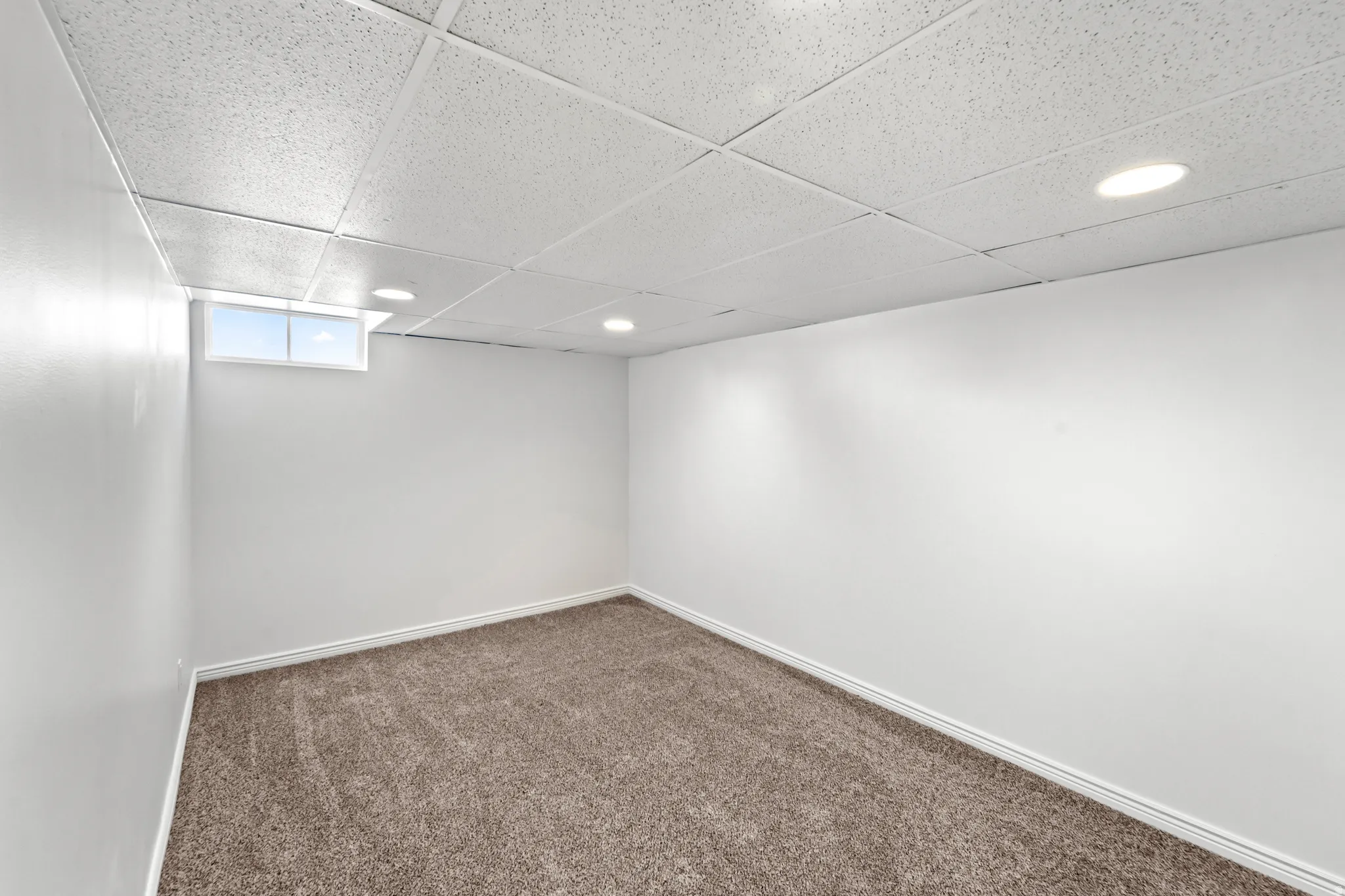 Expansive room featuring clean white walls, a drop ceiling with recessed lighting, and a small window