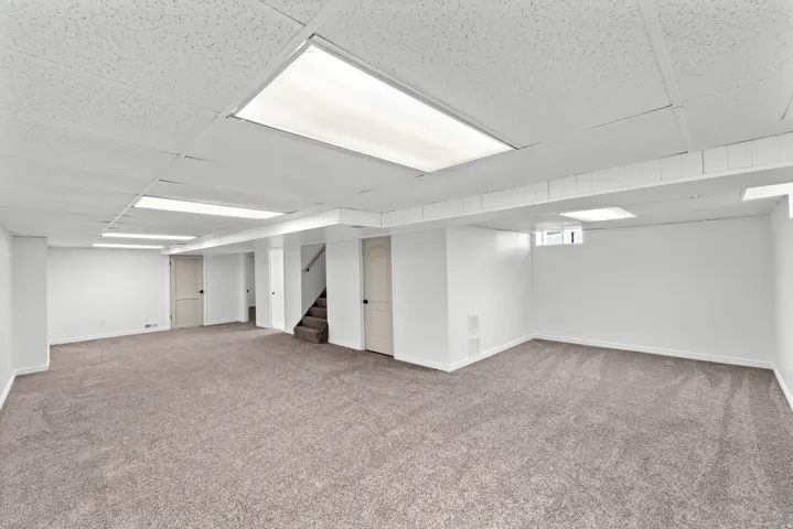 Expansive finished basement featuring neutral-toned carpeting, white painted walls, a dropped ceiling with integrated lighting, and multiple paneled doors
