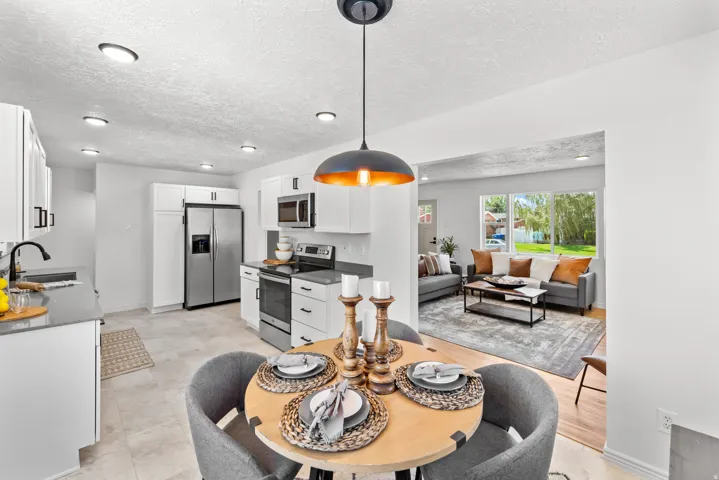 Open-concept living area featuring a kitchen with white cabinetry and stainless steel appliances, a dining area with a modern pendant light, and a living room with large windows