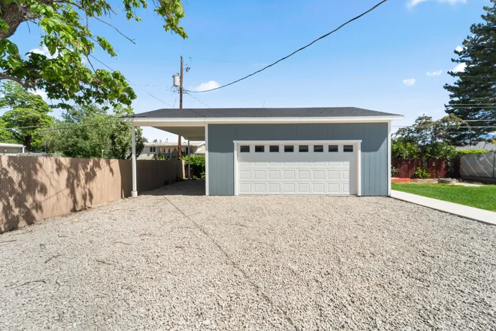 Detached garage with blue siding, white paneled garage door with upper windows, a black shingle roof, and an attached carport