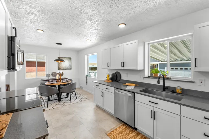 Open-concept kitchen featuring white cabinetry, dark countertops, a stainless steel dishwasher, and a stainless steel sink with a matte black faucet