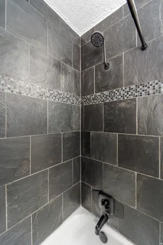Bathtub shower combination featuring dark slate-style tile surround with mosaic accent band, a matte black shower head, and coordinating tub spout with control