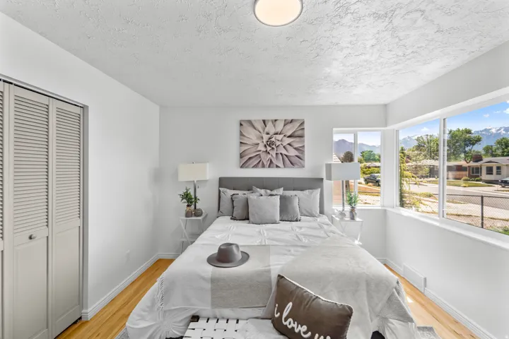 Bedroom featuring expansive windows, wood-finish flooring, white walls, louvered bi-fold closet doors, and a ceiling-mounted light fixture