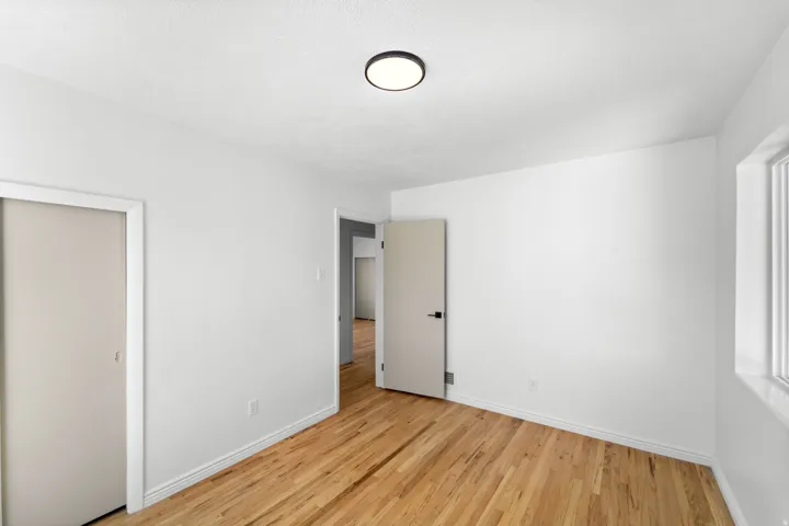 Hardwood flooring throughout this room, featuring a built-in closet with sliding doors, a modern ceiling light fixture, and a window with a deep sill