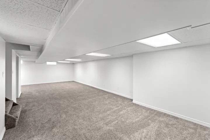Expansive room featuring neutral carpet flooring, white walls, and a combination drop ceiling with integrated rectangular lighting fixtures