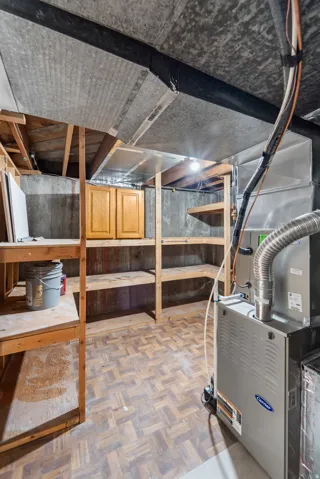 Utility room featuring a Carrier furnace, exposed ductwork, wood-finish flooring, built-in wooden shelving, and built-in wood cabinetry