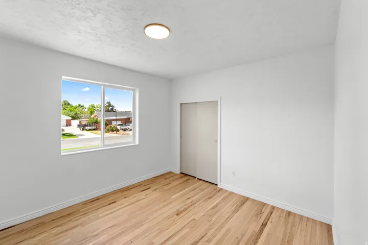 Room featuring wood-finish flooring, a contemporary ceiling light fixture, a large window, and a built-in closet with bifold doors