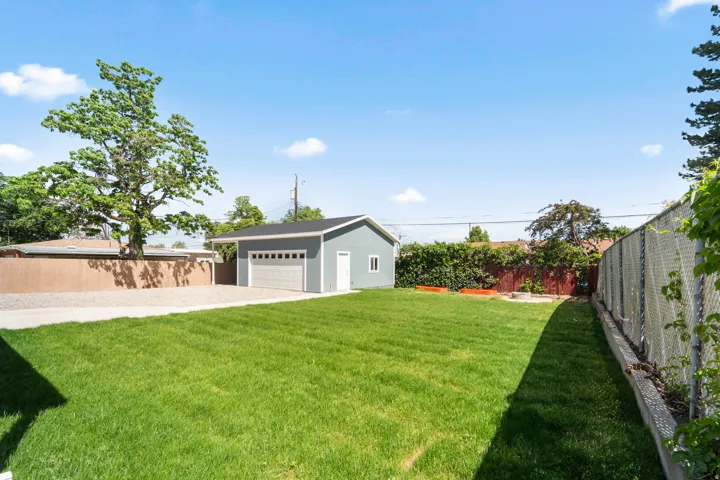 Spacious backyard featuring a detached garage with a paneled door, extensive gravel parking, a vibrant green lawn, and perimeter fencing
