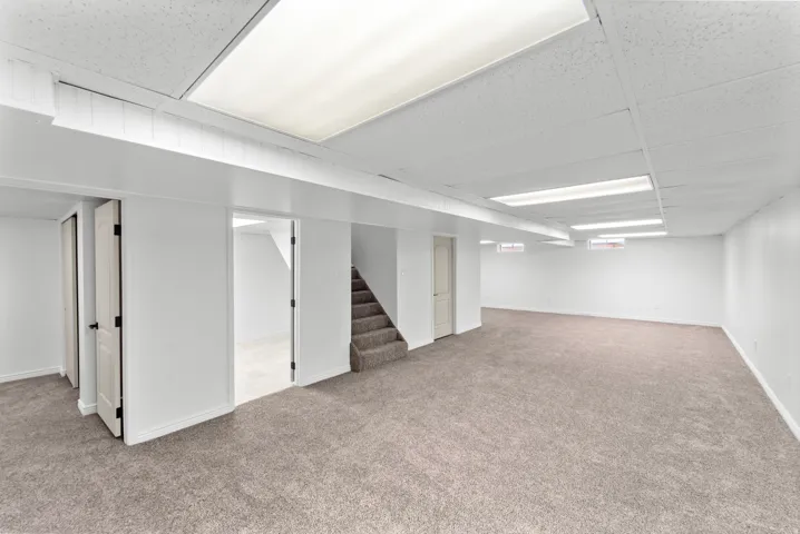 Expansive carpeted area featuring a drop ceiling with integrated lighting, white walls, and a staircase