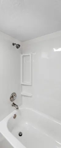 White bathtub and shower combination featuring a built-in shelving niche and brushed nickel shower fixtures