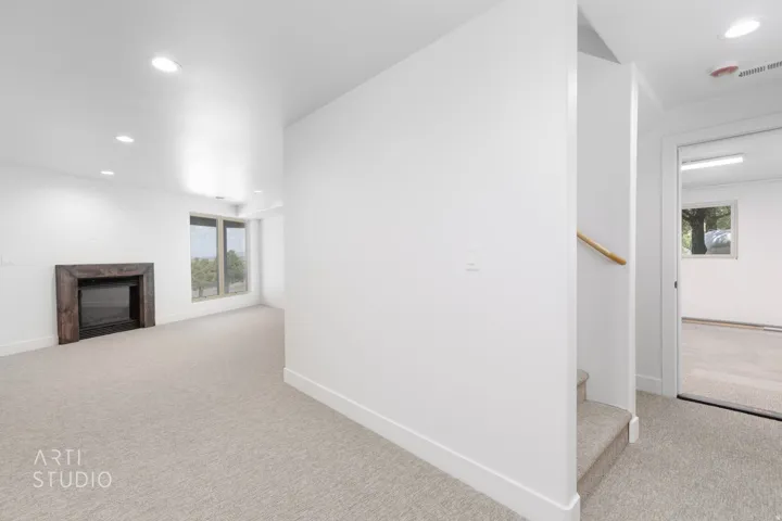 Carpeted living area featuring a dark wood-finish fireplace surround, recessed ceiling lighting, and large windows