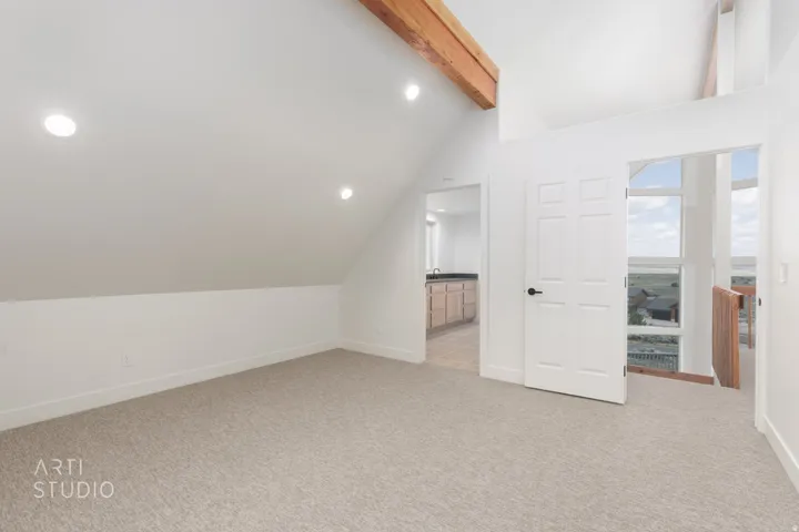 Carpeted room with vaulted ceilings and exposed wooden beams
