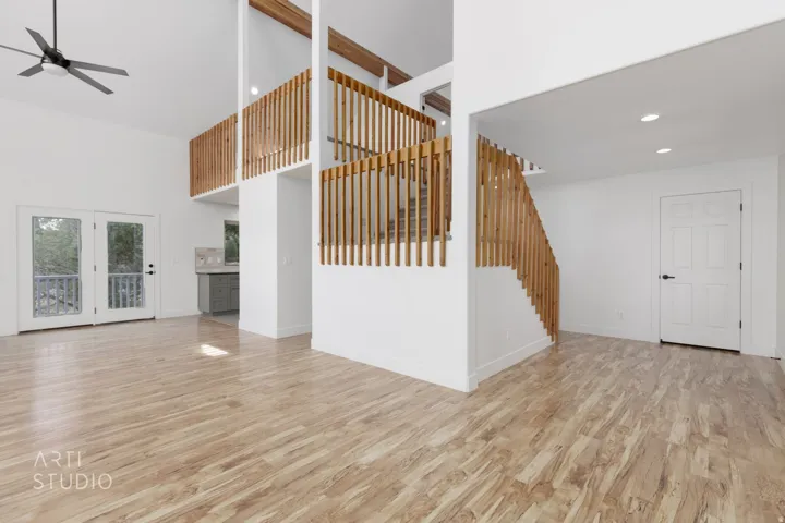 Open-concept interior featuring light wood-finish flooring, soaring vaulted ceilings, and a contemporary ceiling fan
