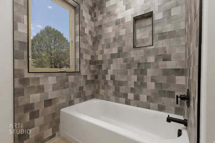 White soaking tub surrounded by variegated gray subway tile