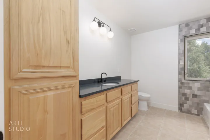 Light wood-finish vanity with ample storage, dark countertop, and single basin sink