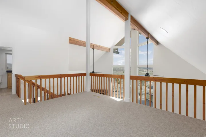 Open loft area featuring a vaulted ceiling with exposed wood beams, a light-toned carpet, and a natural wood railing