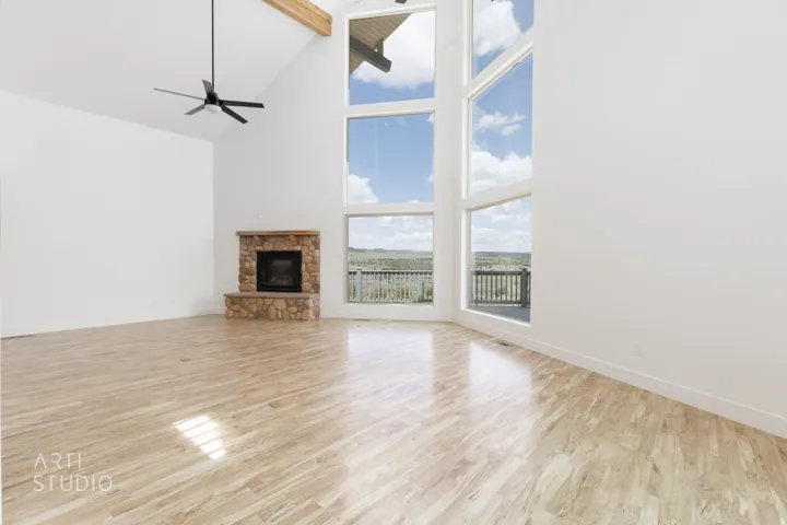 Vaulted ceilings with exposed wood beams, a stone fireplace, wood-finish flooring, and expansive windows offering distant scenery