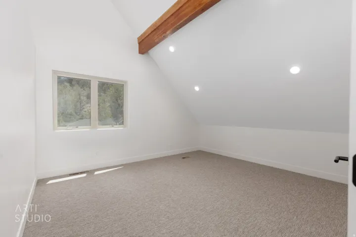 Sloped ceiling room featuring a natural wood beam, recessed lighting, and a neutral carpeted floor