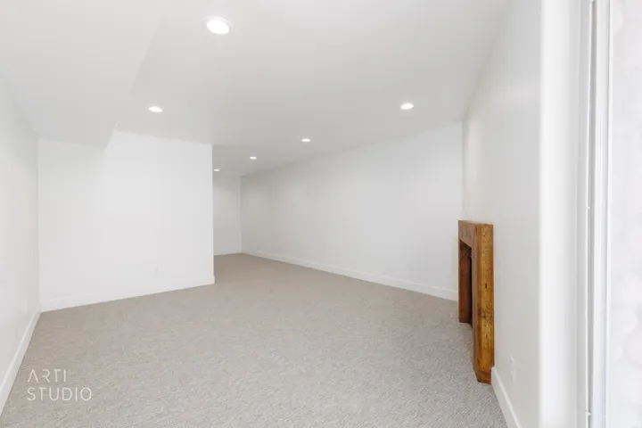 Spacious room featuring neutral carpeting, white walls, recessed ceiling lighting, and a decorative wood mantel