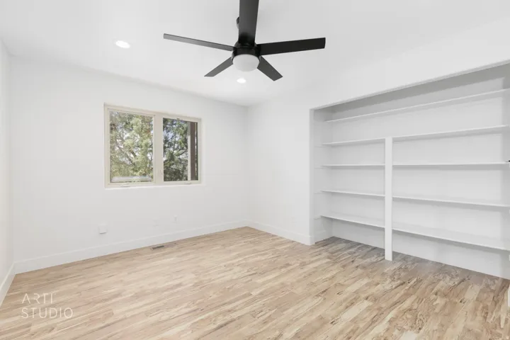 Bright interior space featuring wood-finish flooring, a contemporary ceiling fan, recessed lighting, and a window with exterior tree views