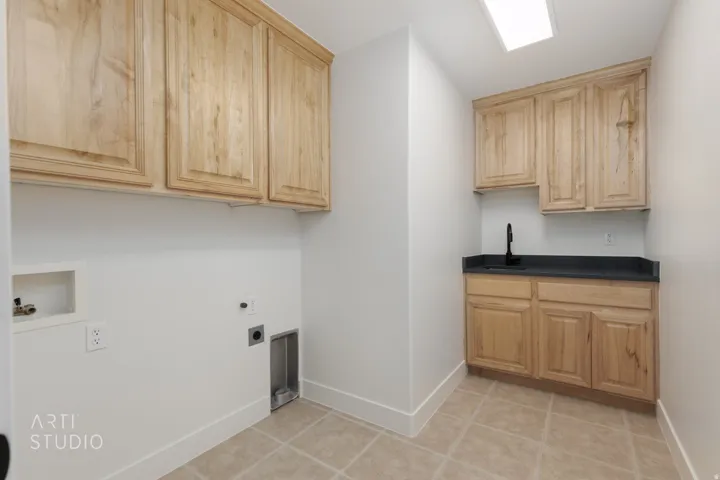 Utility room featuring light wood-finish cabinetry, a black countertop with an integrated sink, and a matte black faucet