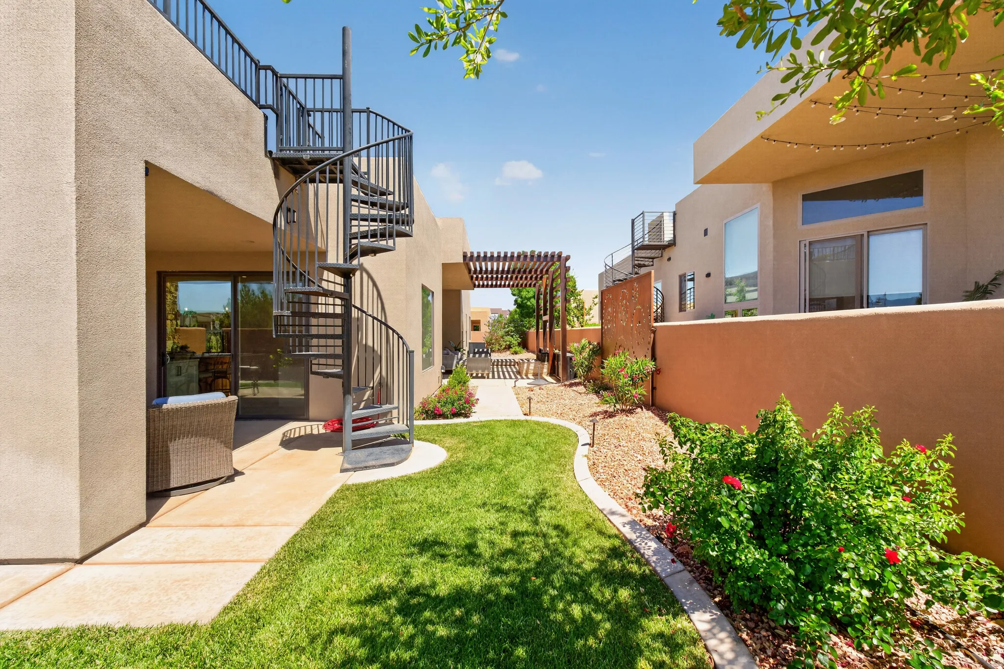 Private exterior patio featuring a black spiral staircase, manicured lawn, and a wooden pergola structure