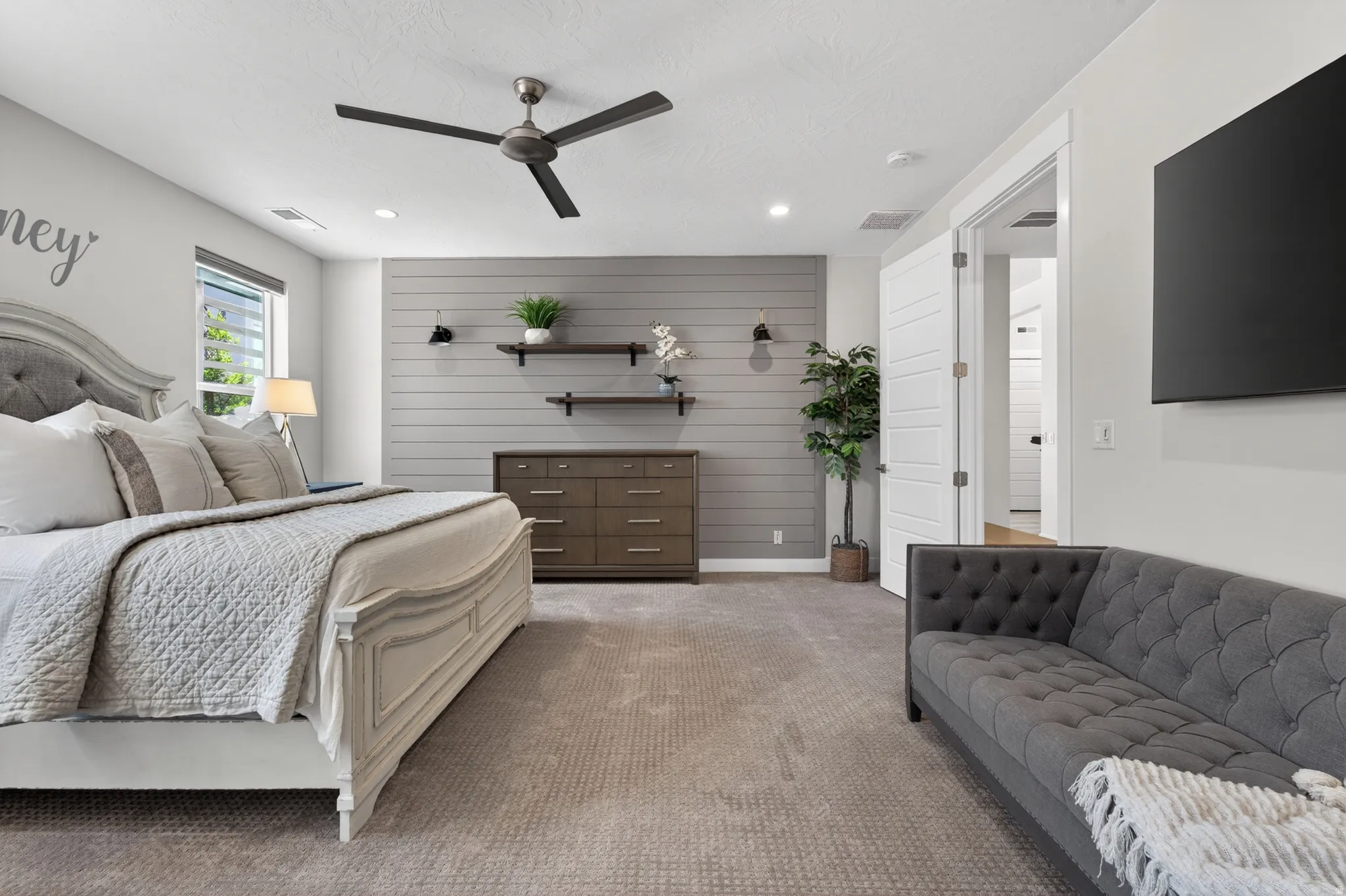 Spacious room featuring neutral carpeting, a modern ceiling fan, and a shiplap accent wall with built-in shelving
