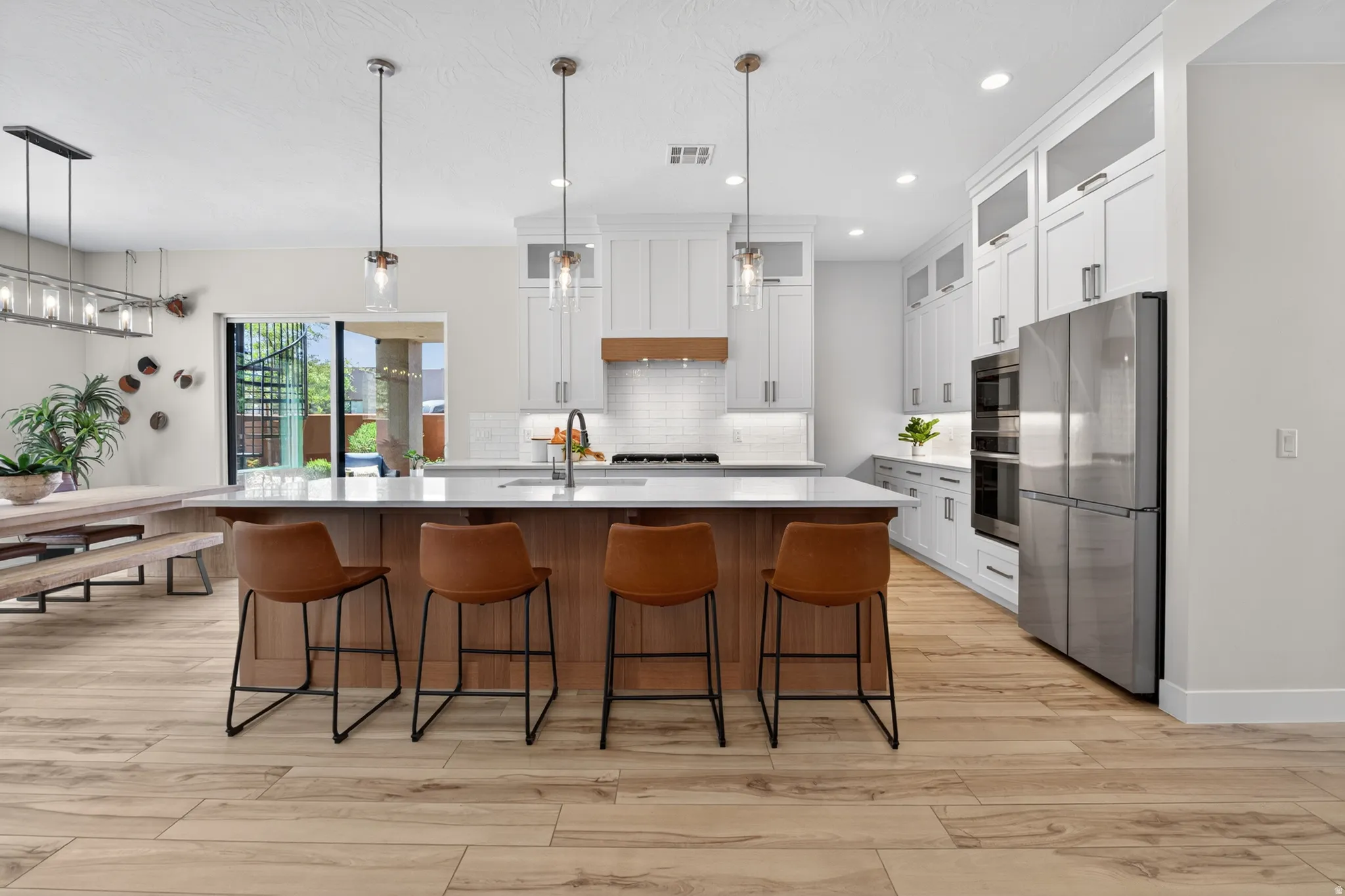 Expansive kitchen featuring a large central island with seating, white shaker cabinetry, stainless steel appliances, and wood-finish flooring