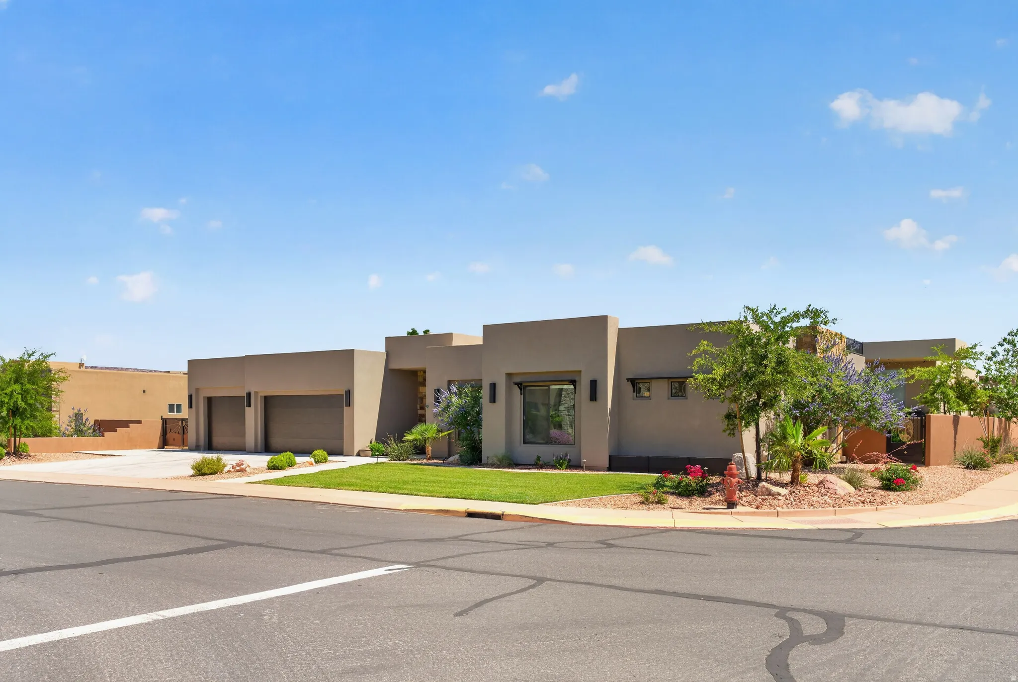 Contemporary stucco exterior featuring a two-car garage, mature landscaping, and a manicured lawn