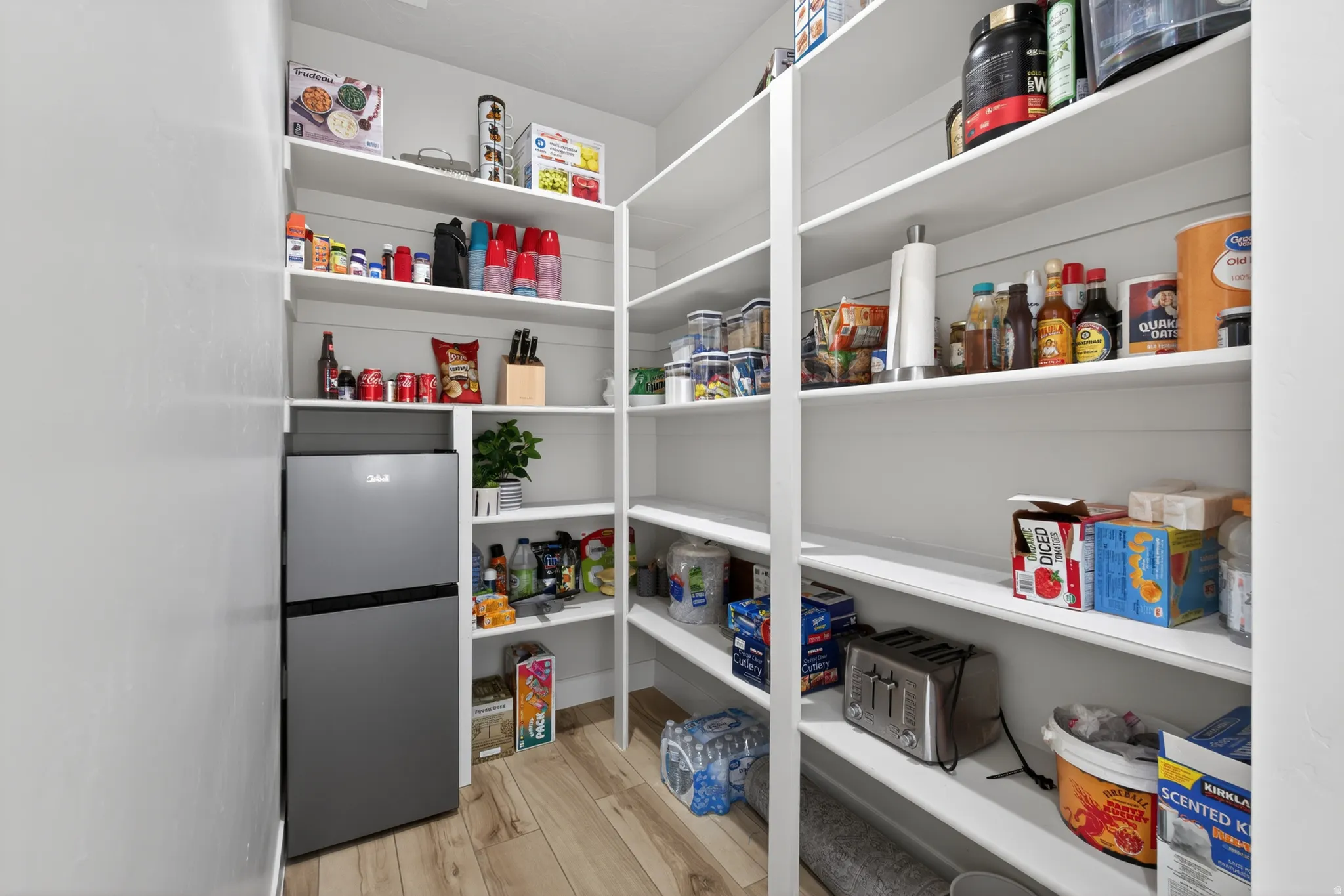 Custom pantry featuring floor-to-ceiling white shelving, a built-in refrigeration unit, and wood-finish flooring